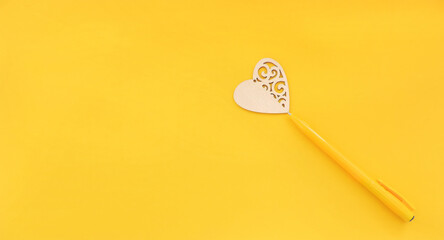  carved wooden heart on yellow background with yellow pen. Concept of love and romance. Beautiful background for Valentines Day. Space for copy space and lettering. Minimalistic   