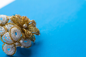 Bouquet with golden flowers from beads on a blue background. Flowers from gold and white beads. Beaded flowers. Handwork. Creative background with place for text. copy space, top view, flat lay