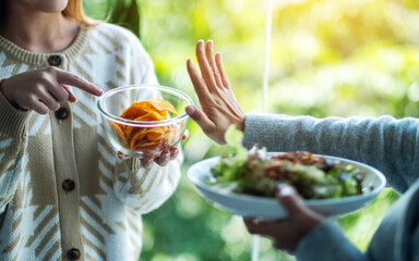 Women choosing to eat vegetables salad and making hand sign to refuse potato chips
