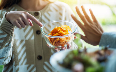 Women choosing to eat vegetables salad and making hand sign to refuse potato chips
