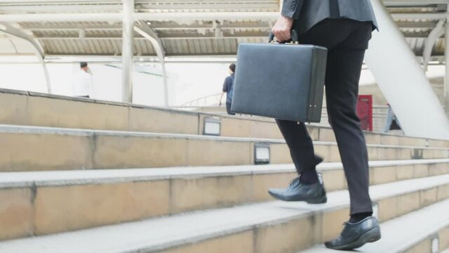 Asian young businessman holding briefcase and walk up the stair.