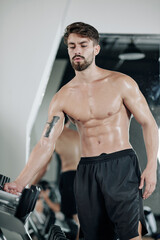 Fototapeta na wymiar Sweaty young fit strong man taking heavy dumbbell from stand in gym