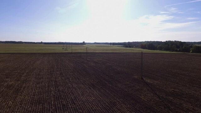 Power Supply Pole Lines In Harvested Agricultural Fields On a Sunny Day. Aerial Flying Forward Footage.
