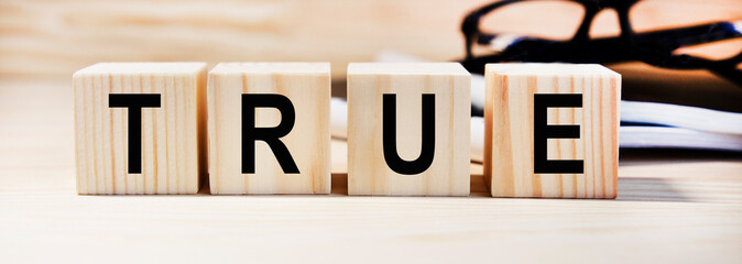 On wooden cubes the text TRUE, in the background glasses, books, reports.