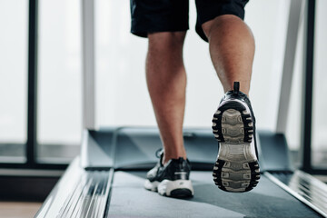 Close-up image of fit man running on treadmill in gym, focus on sneaker sole