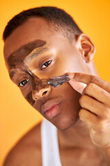 portrait of black african man taking off the facial mask isolated over orange background, young male cares of his skin, get beauty procedures