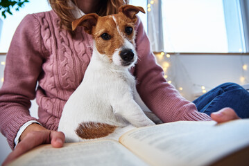 Woman hold dog and reading book. Relaxing together with a pet