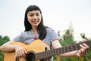 Beautiful young asian woman playing guitar in nature outdoors.