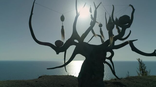 Flight close to dark silhouette Baikal lake keeper sculptural mystical composition wooden tree. Buryat ritual jewelry on branches. Olkhon Uzury village travel attraction. White sun light. Professional