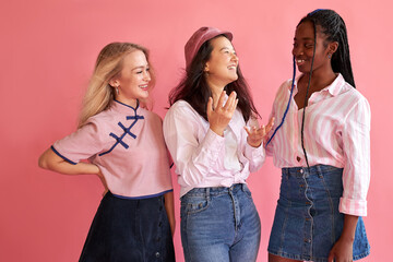 mixed race cheerful women friends posing with smile and have a fun on pink background, wearing trendy casual outfit