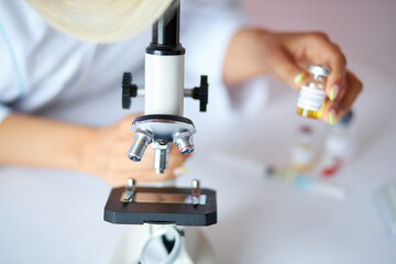 caucasian female scientist holding sampling oil or chemical liquid in flask with lab glassware in laboratory background, coronavirus covid-19 vaccine development