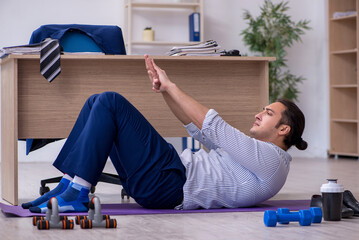 Young handsome male employee doing exercises in the office