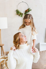 Mother and daughter in light sweaters are sitting on the sofa, the room is decorated for the new year and Christmas, hugs, conversations, smiles, kisses, waiting for a gift and magic