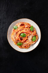 Spaghetti pasta with tomato sauce, Parmesan cheese and fresh basil leaves, shot from above on a dark background with a place for text