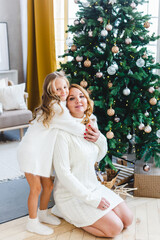 A girl with her mother near the Christmas tree, the interior decorated for the new year and Christmas, family and joy, traditions