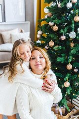 A girl with her mother near the Christmas tree, the interior decorated for the new year and Christmas, family and joy, traditions