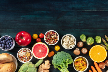 Healthy organic vegetarian food, overhead shot with copy space. Fruit and vegetables, legumes, cheese and other products, a flat lay on a dark background