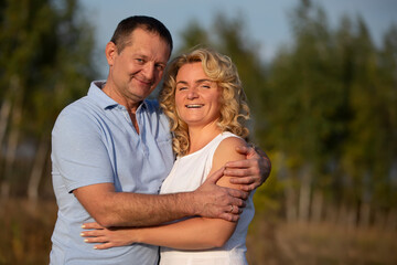 A beautiful middle-aged couple in love are hugging and looking at the camera.