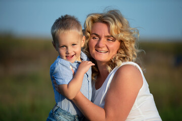 Fototapeta na wymiar Happy mom with her son outdoors. Blonde European style woman hugs little boy.