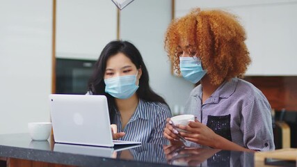 Two young women asian and black with face masks browsing social media on the laptop. High quality 4k footage - Powered by Adobe