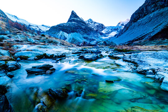 Close up of a river flowing through a valley in late autumn with snow capped mountains in the background