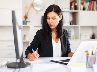 Smiling woman working with papers and laptop in office