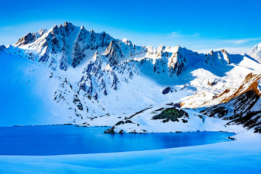 A frozen lake surrounded by snow capped mountains in the Swiss Alps in early morning light