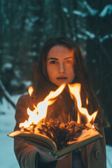 Young female model holding burning open book in the woods.