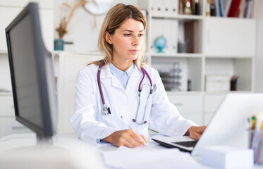 Woman doctor sitting at workplace with computer in her office