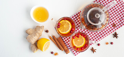 Winter hot tea to strengthen the immune system. Two cups and a glass kettle with tea, lemon, ginger and cranberries on a light background. View from above.