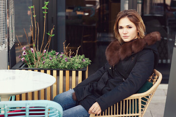  business woman in fox fir dawn jacket with hood close up photo on city open air cafe background