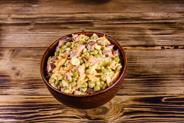 Salad with sausage, green pea, onion and carrot in glass bowl on wooden table