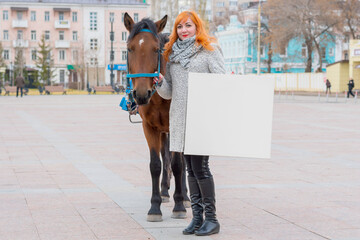 A young red-haired girl holds a horse under the knots with one hand, and in the other holds a blank canvas for painting