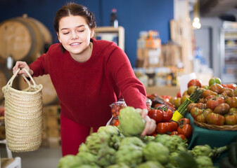 cheerful young girl looking artichokes in grocery market