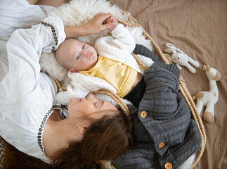 Sleepy baby in a wicker cradle in warmth near a happy caring mother. Happy motherhood concept