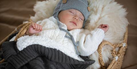 The baby sleeps sweetly in a wicker cradle in a warm knitted hat under a warm blanket. Carefree baby sleep concept.