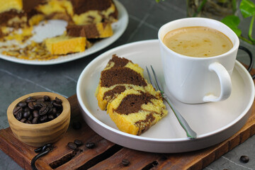 Marmer Cake or marbel Cake on white ceramic on ceramic white plate with a fork, served with a cup of coffee. Black marble background. Selective focus.