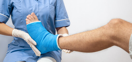Female doctor in a blue medical gown checking broken leg on male patient.