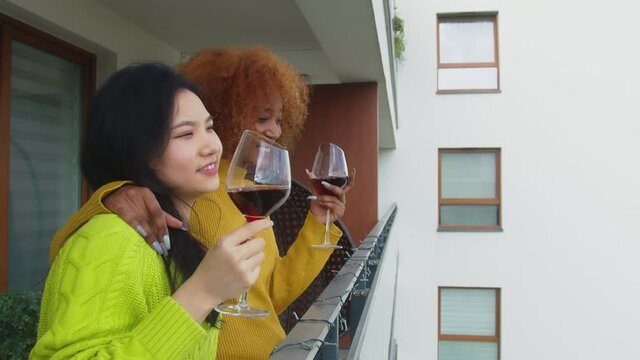 Couple Of Young Interracial Women, Best Friends Or Lesbian Couple, Drinking Wine On The Balcony Singing And Dancing. African American Woman Stroking Hair Of Her Asian Partner. High Quality 4k Footage