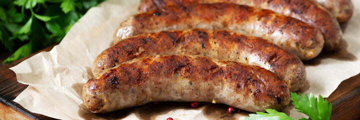 Fried sausages. Grilled sausages with spices on a wooden serving Board. Delicious meat sausages. Banner	