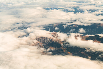 Aerial airplane view over Bucegi Mountains in Romania with mixed autumn winter landscape between the clouds