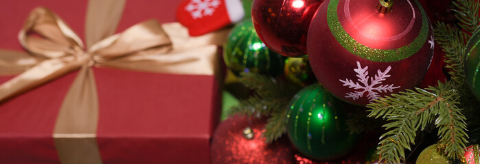 New year's gifts in red wrapping paper with gold ribbons under a Christmas tree decorated with red and green balloons: place for text, top view, christmas banner