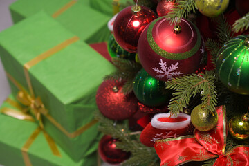 New year's gifts in green wrapping paper with gold ribbons under a Christmas tree decorated with red and green balloons: place for text, top view