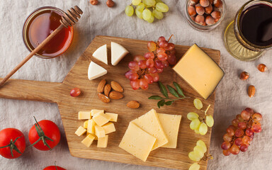 Cheese plate. Assorted cheeses on a wooden Board with grapes, honey, nuts on a linen tablecloth.