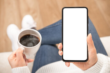 woman's hand holding white mobile phone with blank desktop screen and coffee cup.