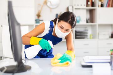 Positive young kazhahstani woman wearing uniform and mask cleaning at company office ..