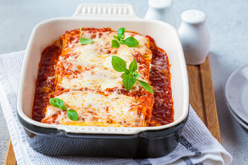 Traditional cannelloni with ricotta and spinach in tomato sauce in ceramic dish. Italian food concept.