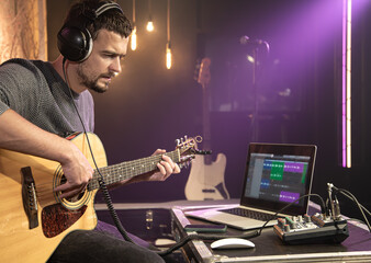 Fototapeta na wymiar European man plays the guitar while recording a track in a music studio.
