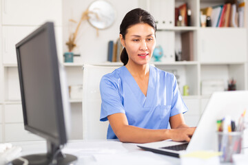Kazhahstani female doctor in uniform is working behind laptop in hospital