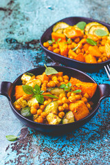 Baked sweet potato, zucchini and chickpeas in cast iron pan, blue background. Baked vegetables....
